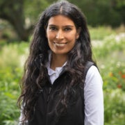 A woman smiles for a photo against a verdant background.