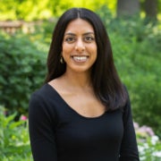 A woman smiles for a photo against a verdant background.