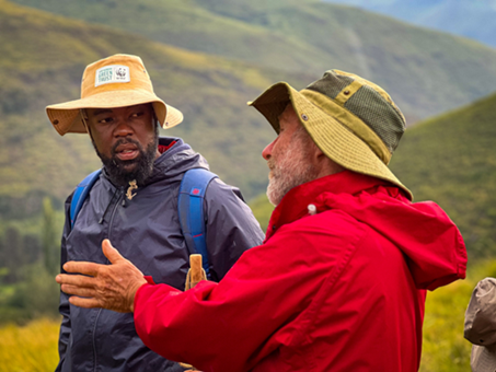 Two people in rain gear engage in a discussion while standing outside in the mountains of South Africa.