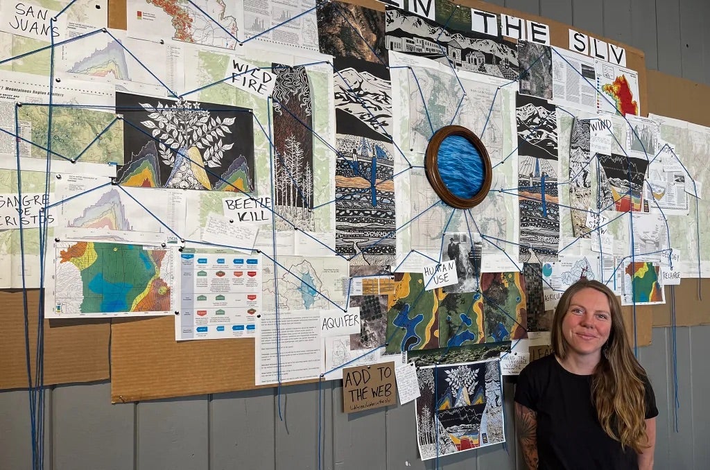 Jocelyn Catterson stands against a backdrop of a wall-sized collaborative art project depicting the connections between various environmental factors and the valley's hydrology. 
