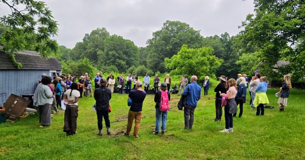 A group stands in a circle in a field at a trip to the Kinston Land Trust farm.