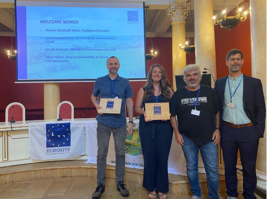 Four people pose for a picture, two holding award plaques. 