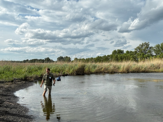 One man wades in a shallow natural pool while two others look on from the shore.