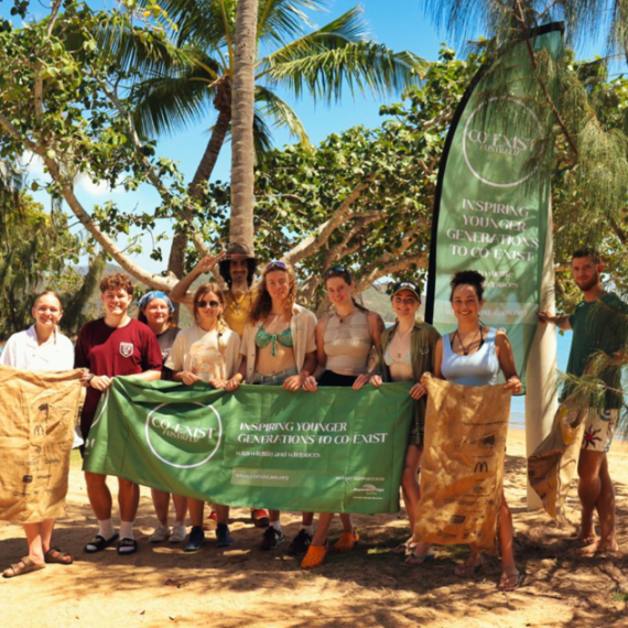10 young people hold a banner in a tropic beach setting.