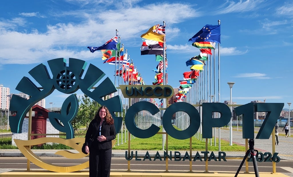 A woman smiles in front of a sign that reads "UNCCD COP17 Ulaanbaatar 2026."
