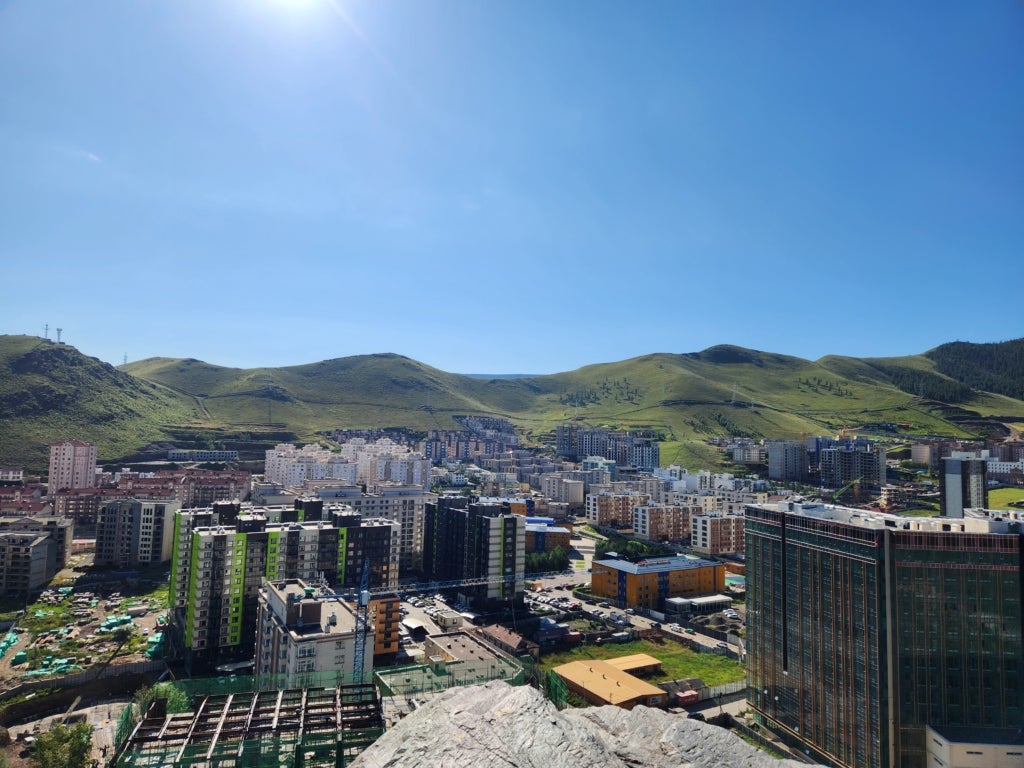 Cityscape with skyscrapers against a verdant mountainous background.
