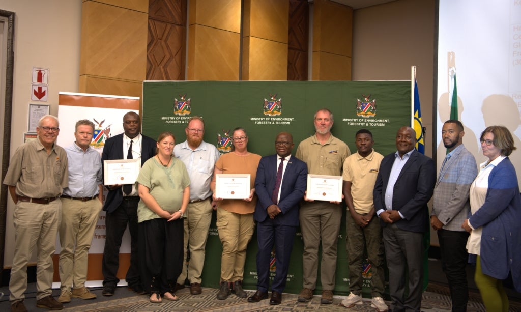Twelve people pose for a photo, three of whom hold certificates.