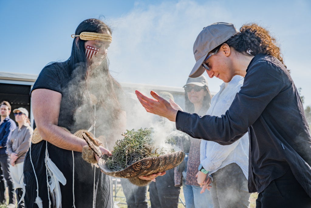 A woman takes in the aroma of burning herbs, held by another woman.